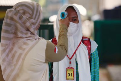 An elementary school student wearing a face mask has her temperature checked before attending a classroom session, as schools reopen amid COVID-19 in Bekasi, on the outskirts of Jakarta, 24 March 2021 (Photo: Reuters/Willy Kurniawan).